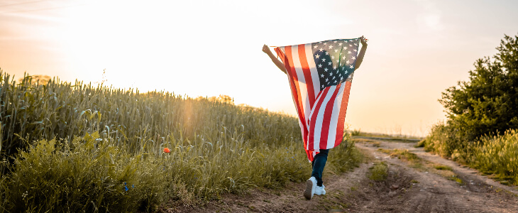 person running through a green field holding up an american flag about us