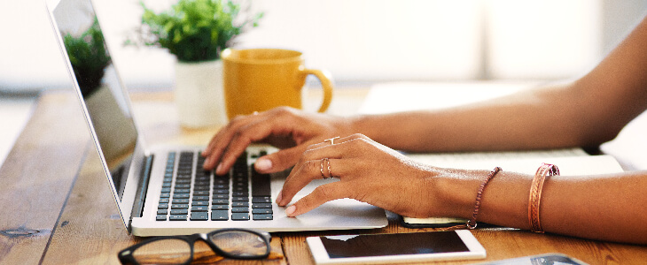 woman wearing rings and bracelets typing on a computer on a table green card